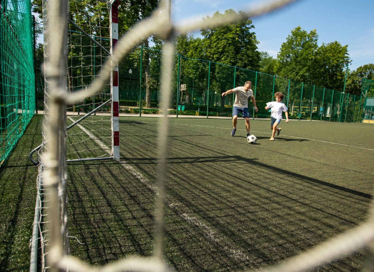 Sportive man playing football with little boy